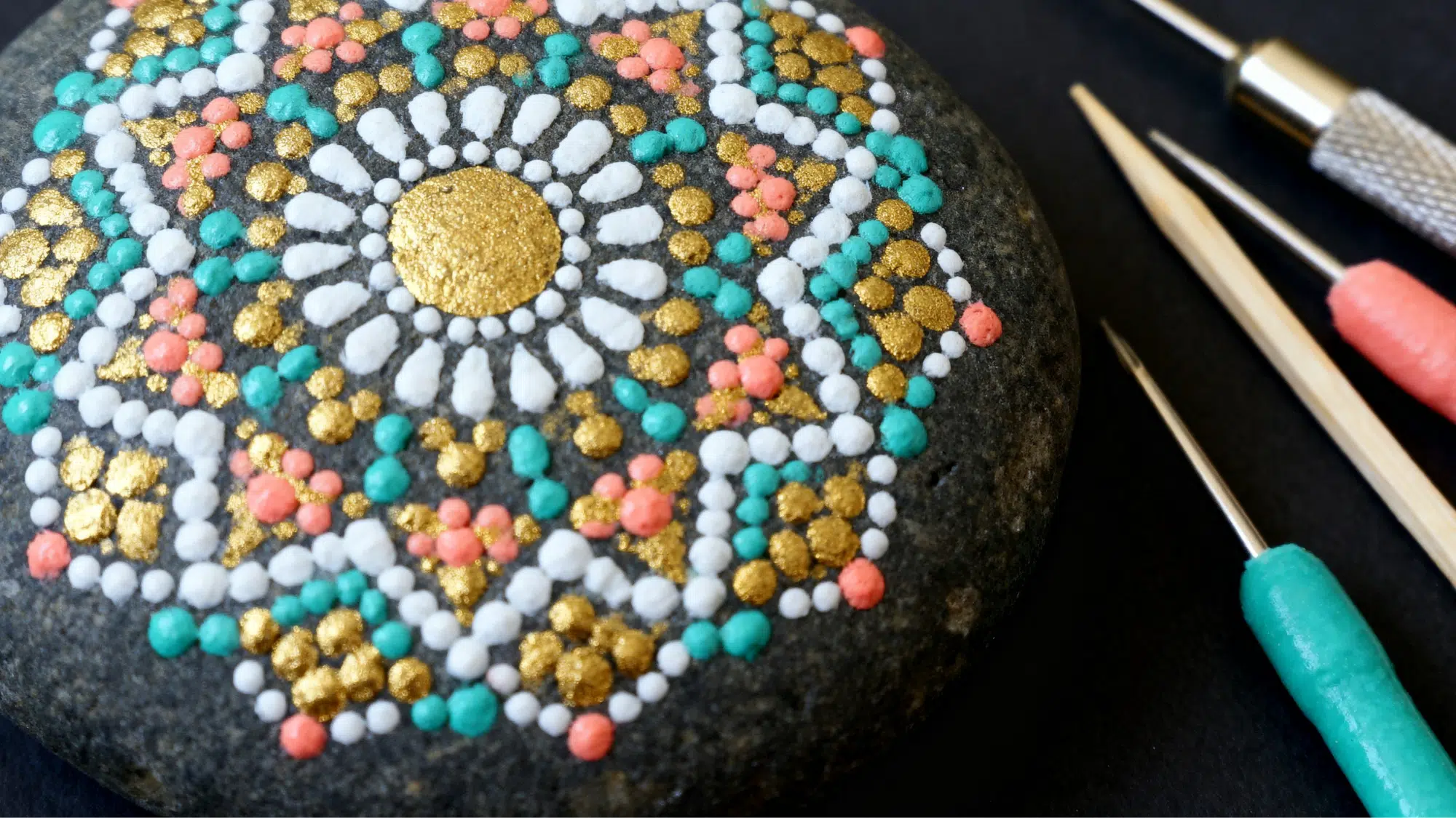 Intricate dot mandala painted rock with gold and teal dots