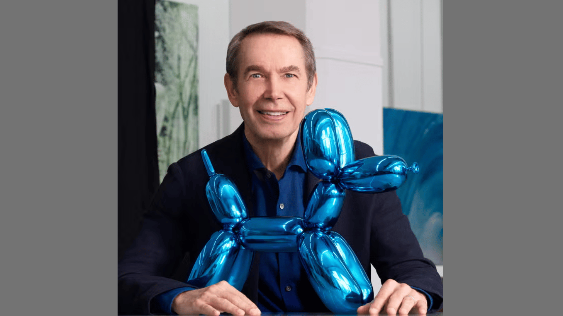 Portrait of artist Jeff Koons in a dark blazer with a blue balloon dog sculpture in front