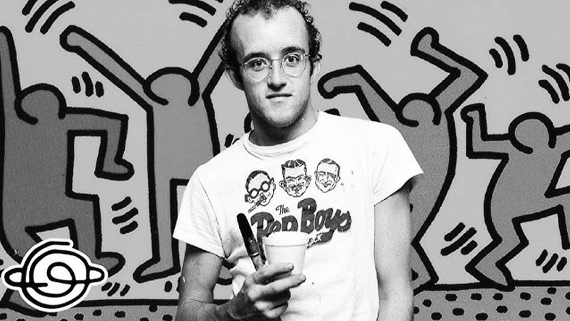 black and white portrait of artist Keith Haring in a graphic T-shirt with his signature dancing figures background