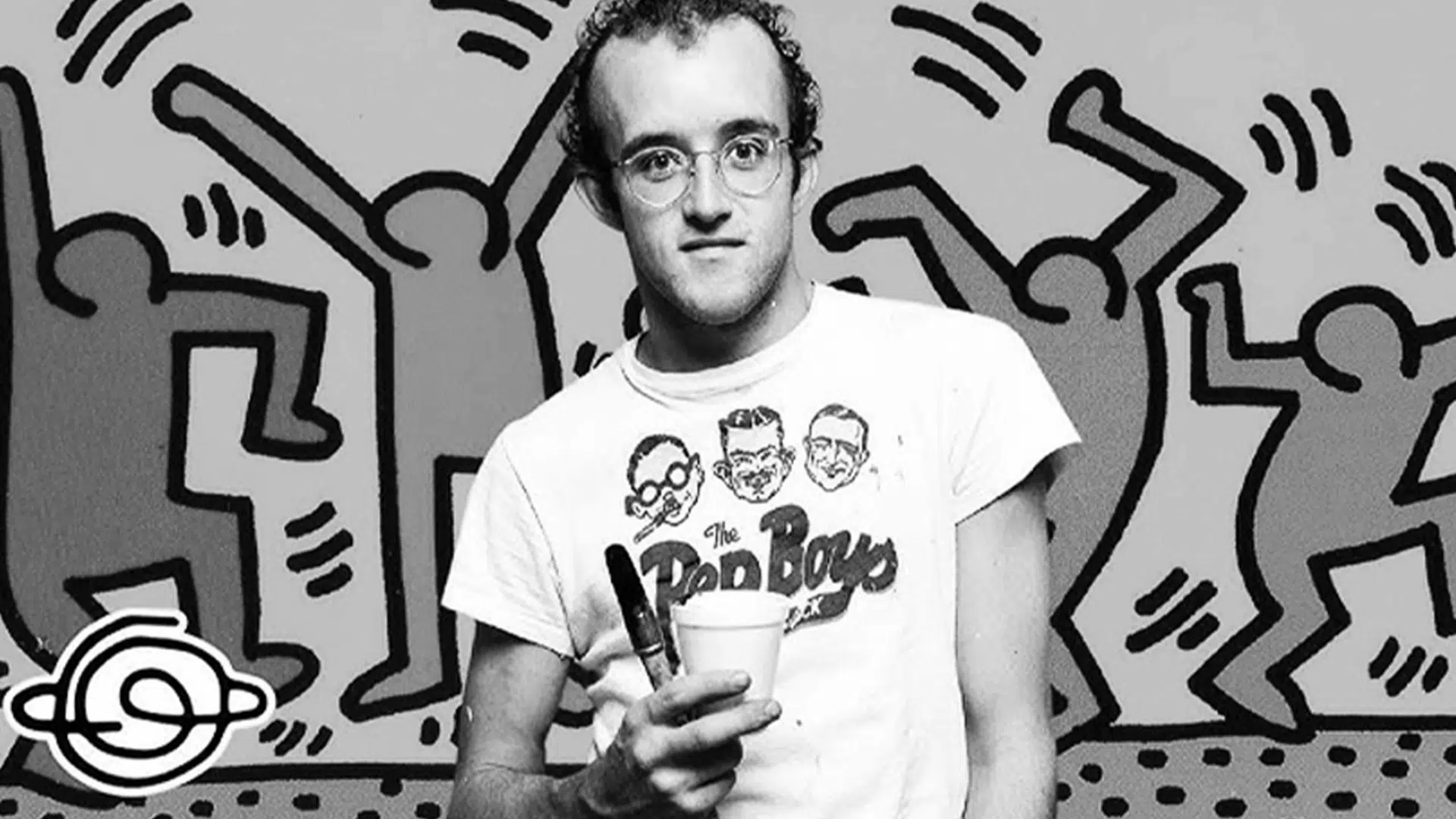 black and white portrait of artist Keith Haring in a graphic T-shirt with his signature dancing figures background