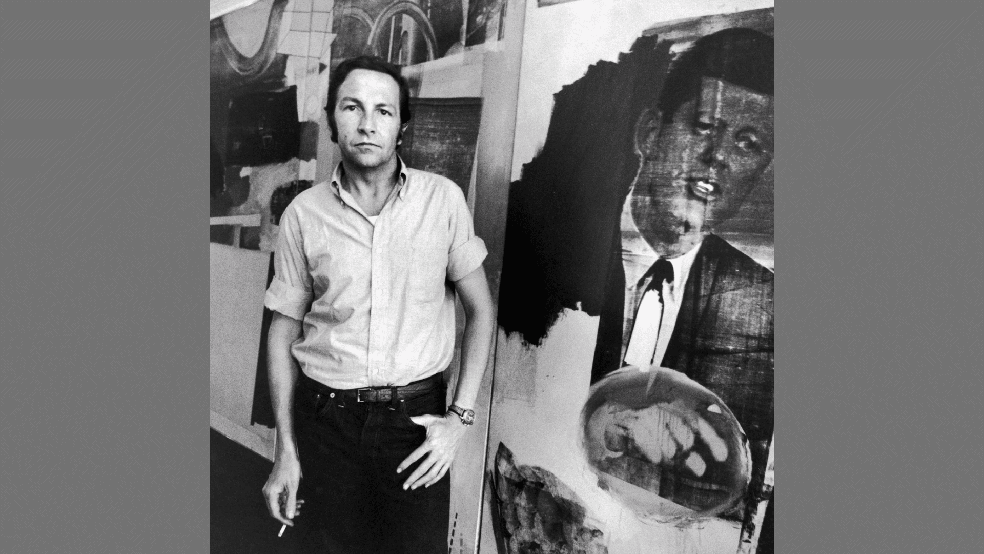 black and white portrait of artist Robert Rauschenberg standing next to his artwork featuring JFK