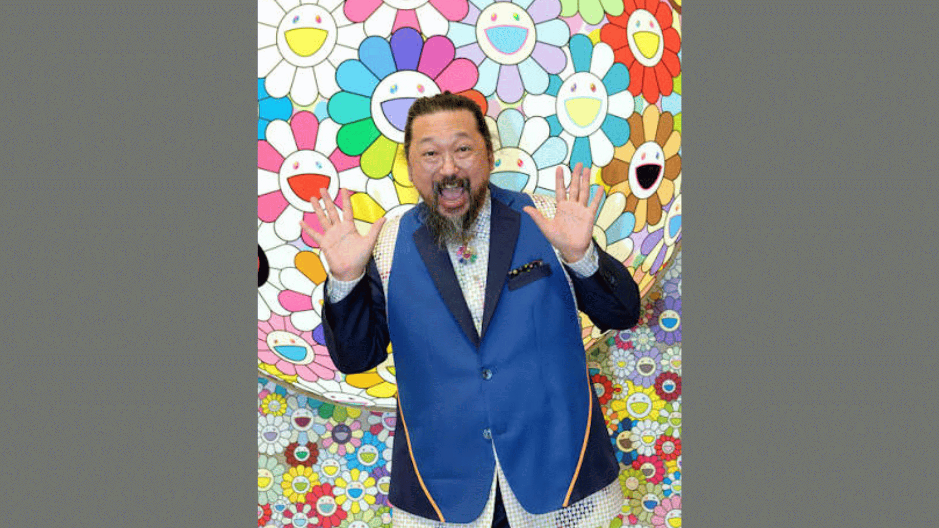 artist Takashi Murakami posing expressively in front of a colorful backdrop covered with his smiling flowers