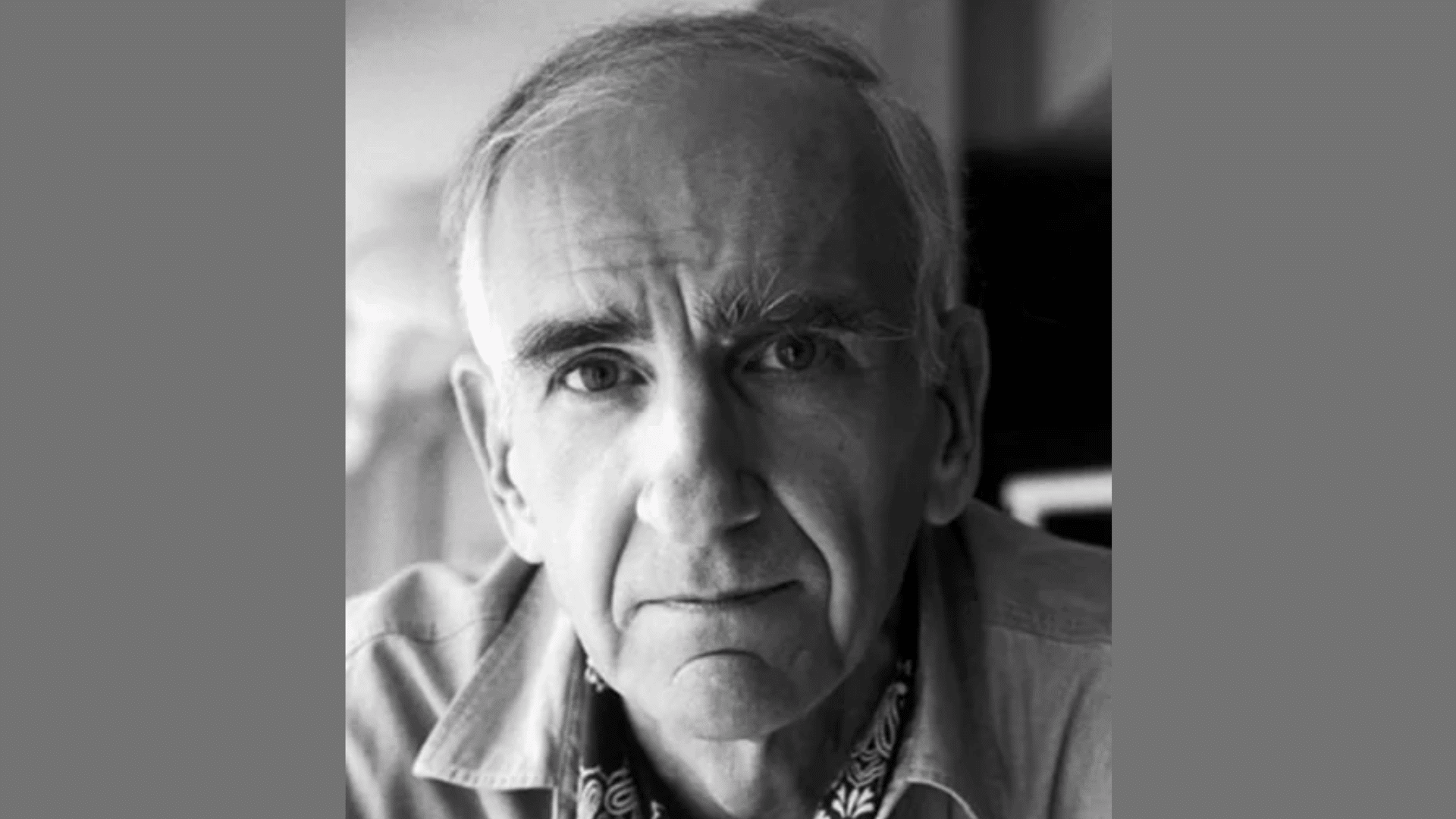 a close-up black-and-white portrait of an older man with bushy eyebrows wearing a patterned neckerchief
