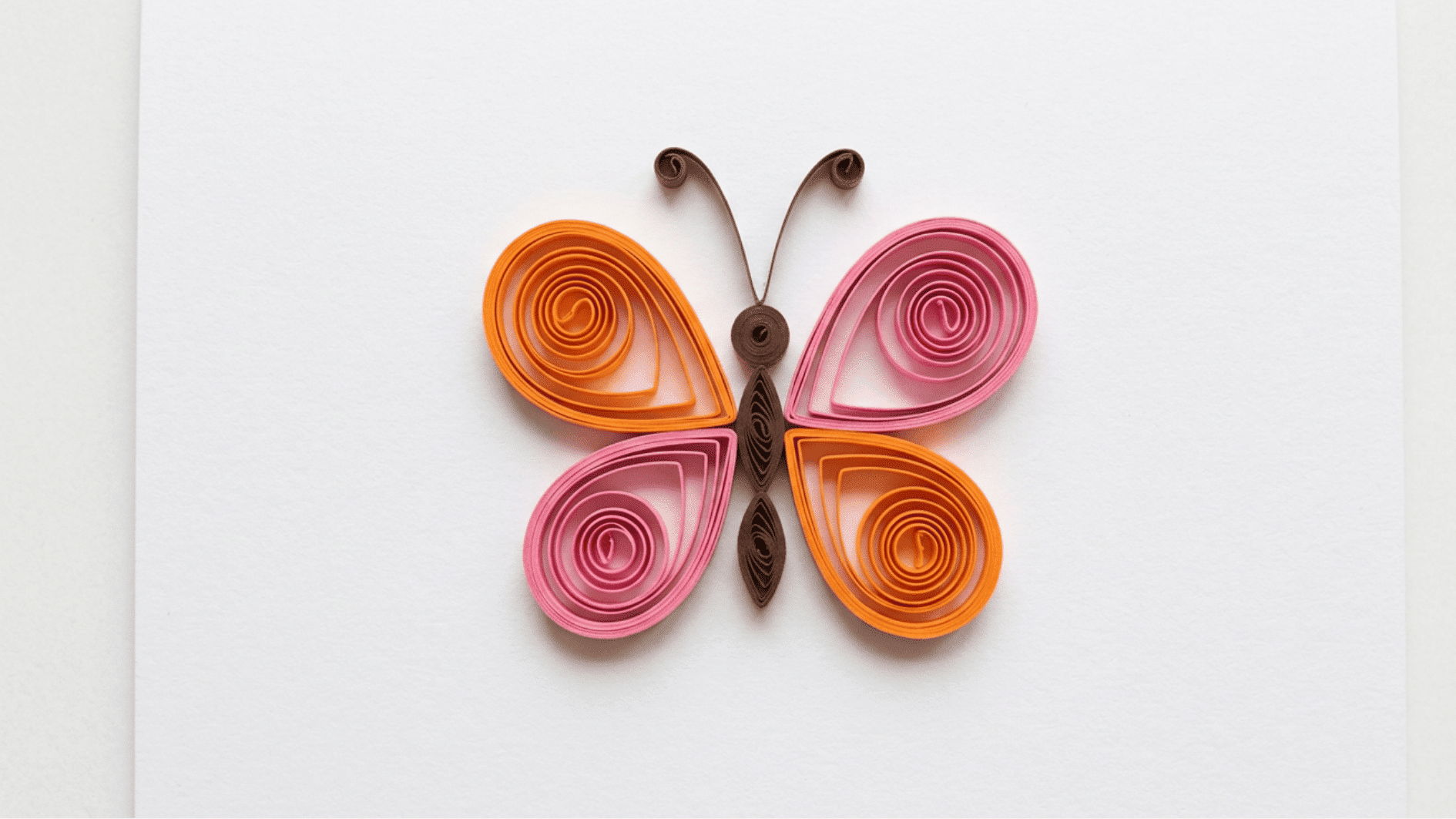 quilled paper butterfly with orange and pink wings and brown body on white background