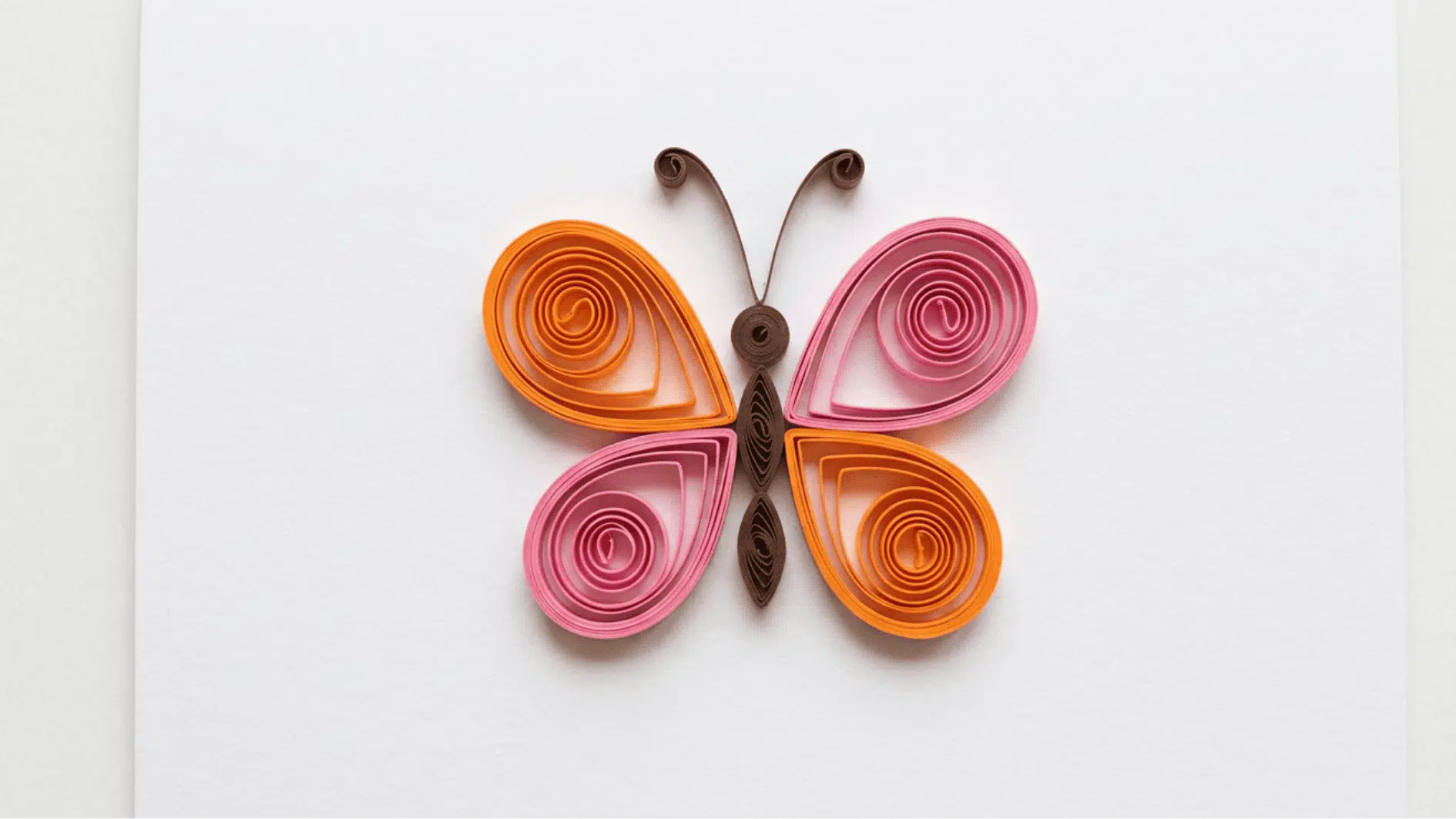 quilled paper butterfly with orange and pink wings and brown body on white background