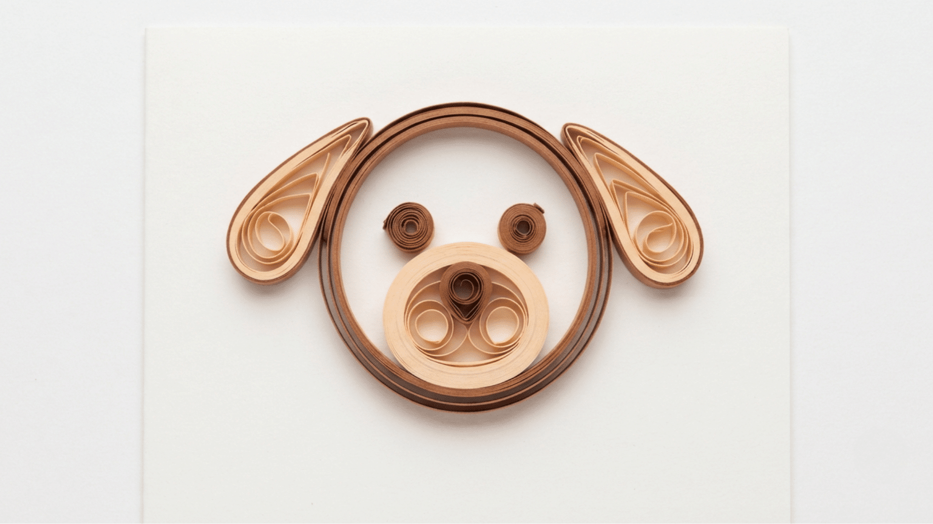 quilled paper dog face in brown and tan with round eyes floppy ears and coiled snout on white background