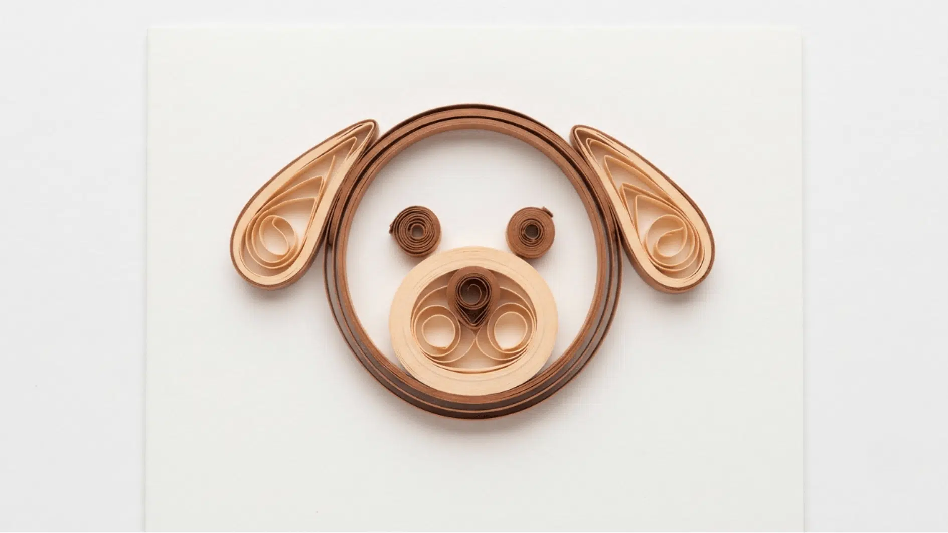 quilled paper dog face in brown and tan with round eyes floppy ears and coiled snout on white background