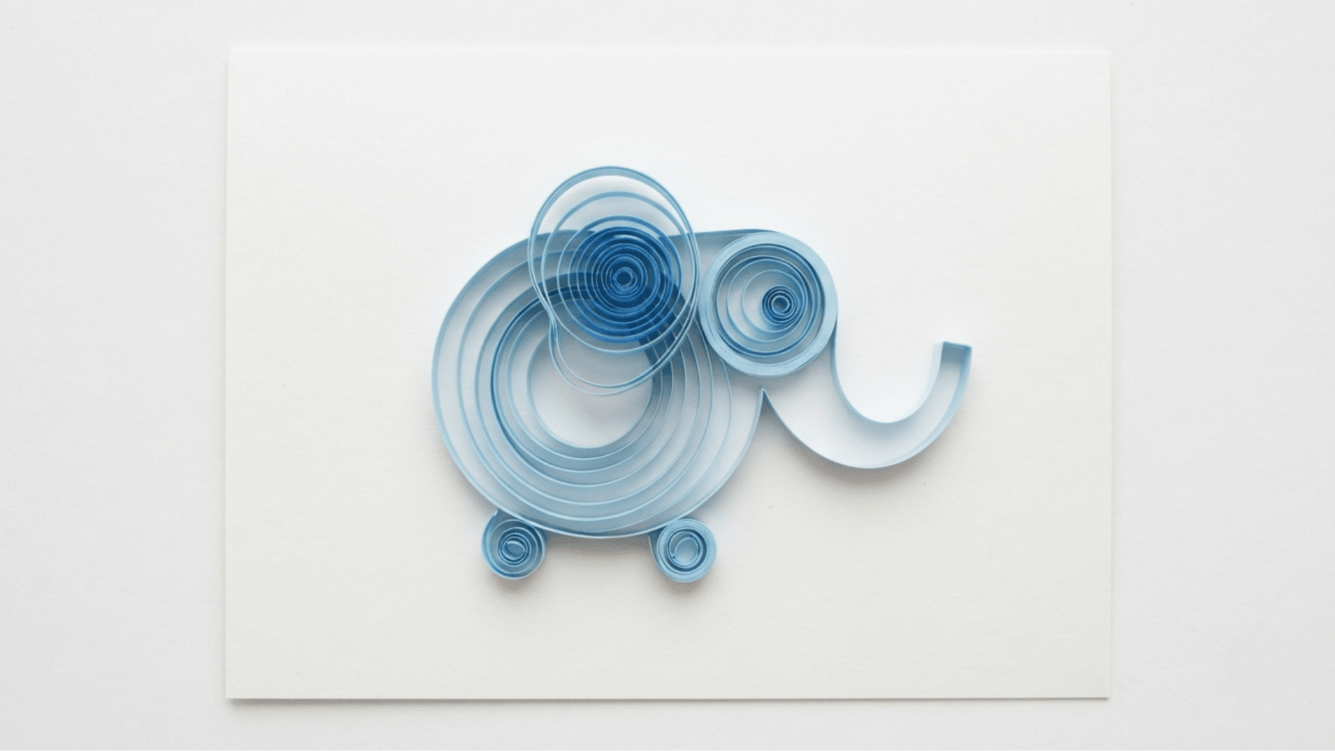 quilled paper elephant in blue coils with curled trunk and ear on white background