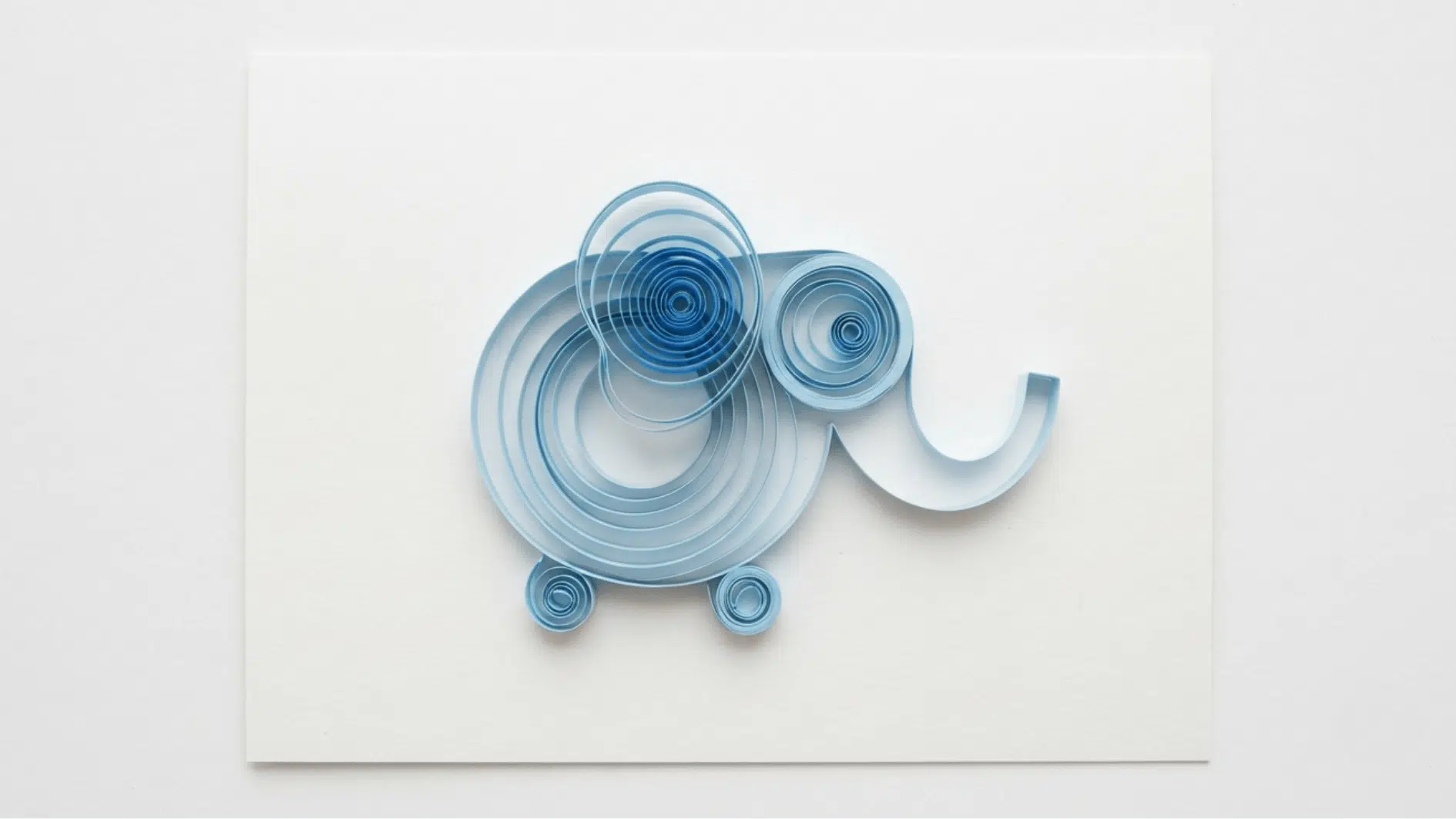 quilled paper elephant in blue coils with curled trunk and ear on white background