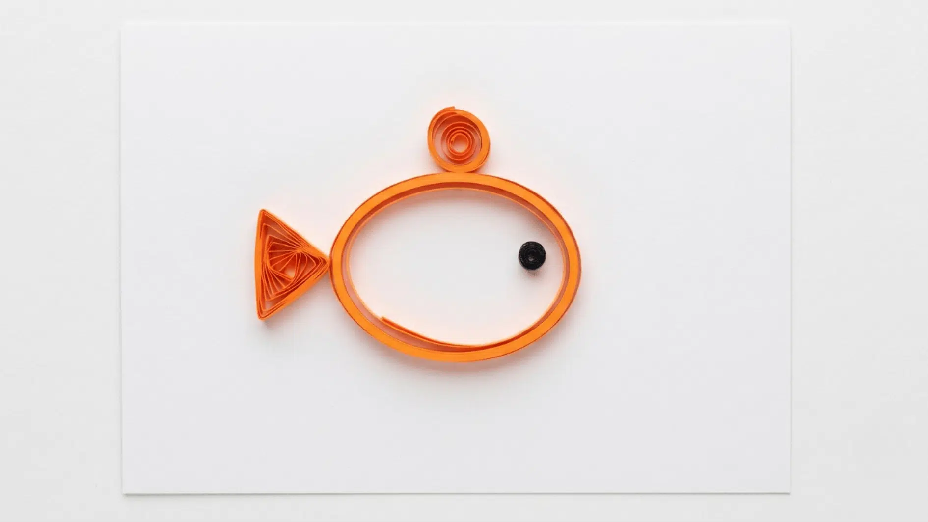 quilled paper fish outline in orange with black eye and triangular tail fin on white background