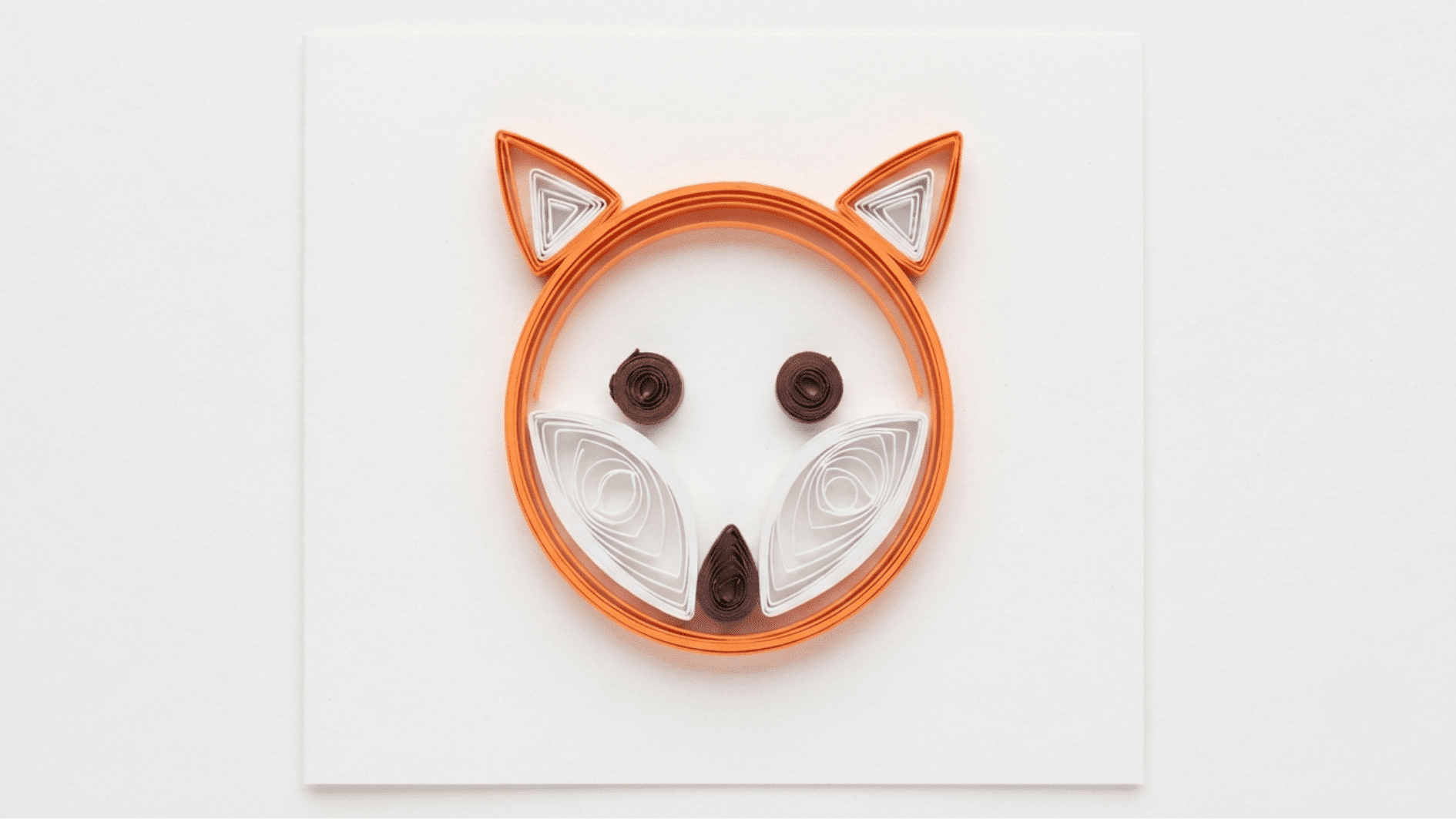 quilled paper fox face in orange and white with brown eyes and nose on white background