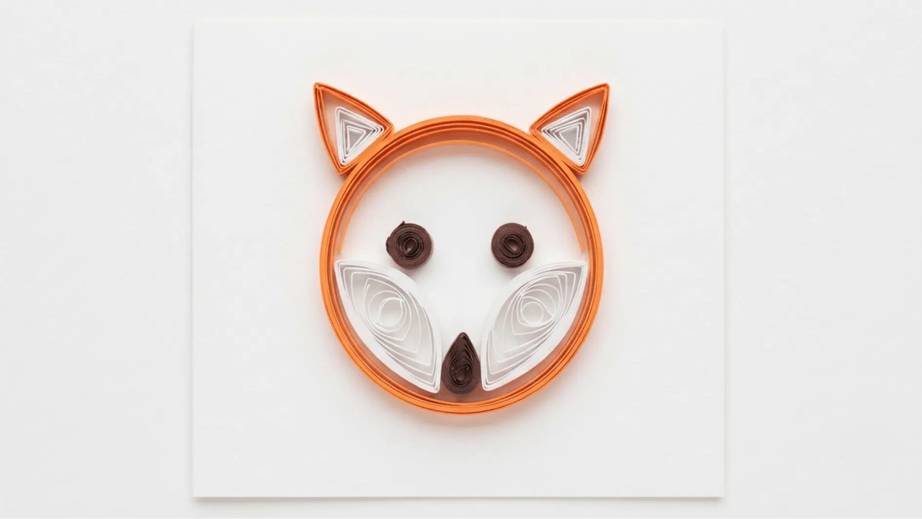 quilled paper fox face in orange and white with brown eyes and nose on white background