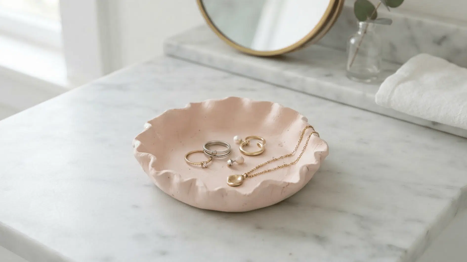 handmade pink clay trinket dish holding rings earrings and a necklace on a marble vanity