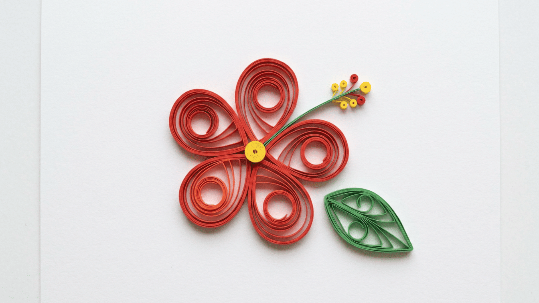 quilled paper hibiscus flower in red with yellow center and stamen and green leaf on white background