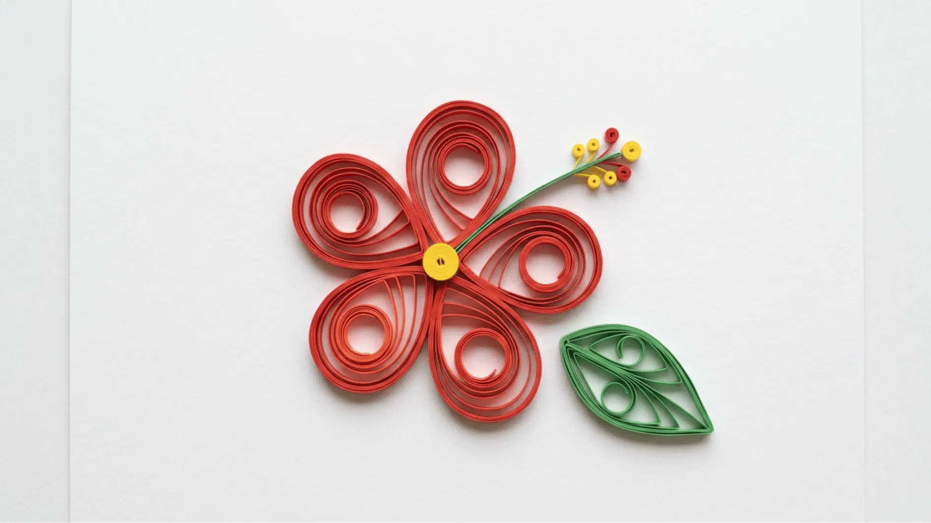 quilled paper hibiscus flower in red with yellow center and stamen and green leaf on white background