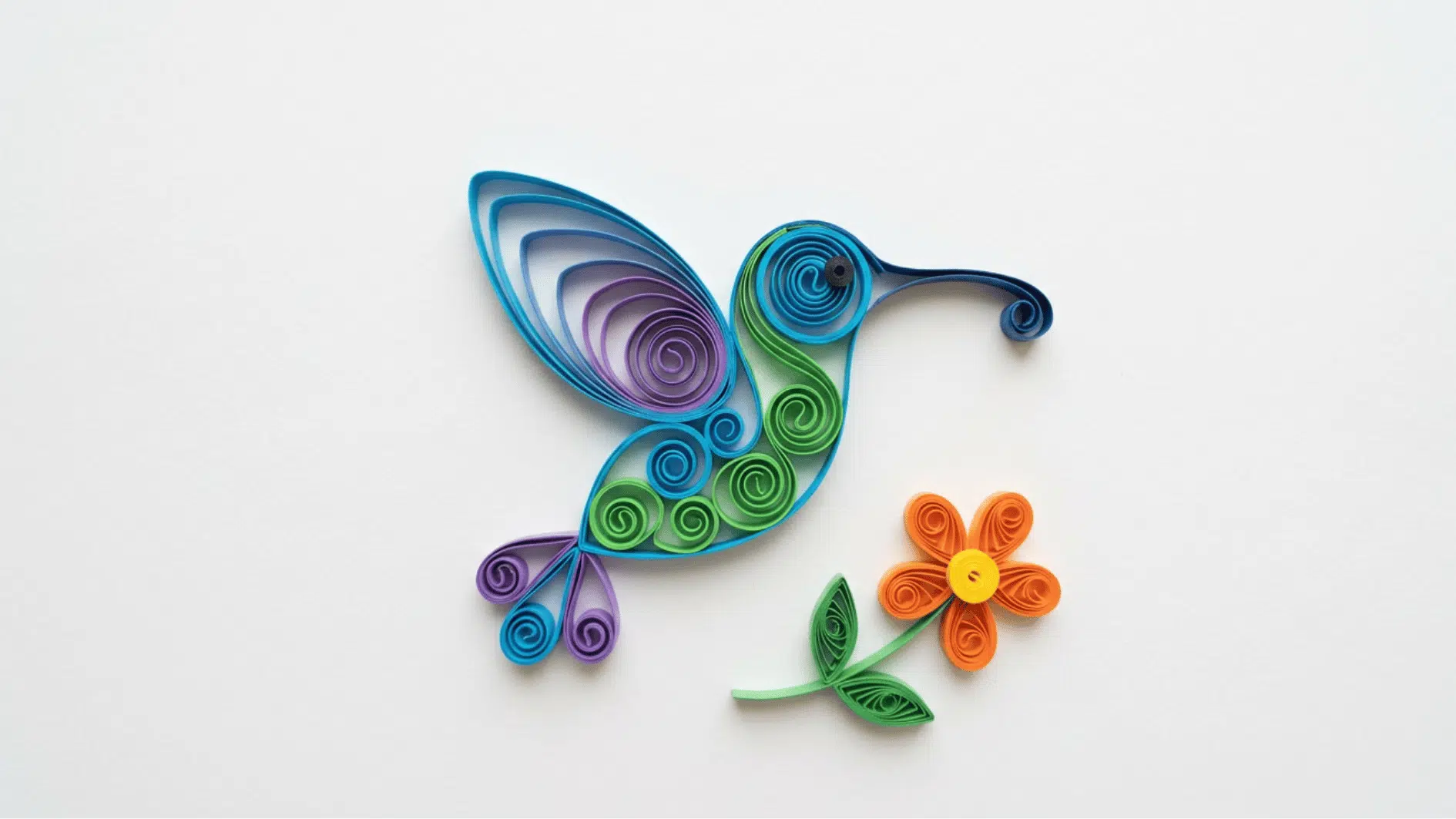 quilled paper hummingbird in blue green and purple with an orange flower on white background