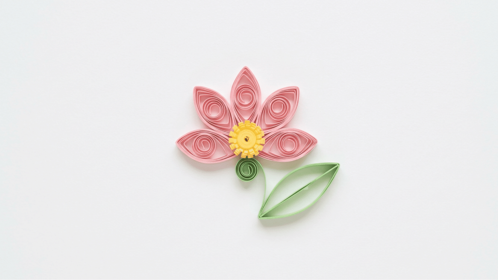 quilled paper flower with pink petals yellow center and curled green stem and leaf on white background