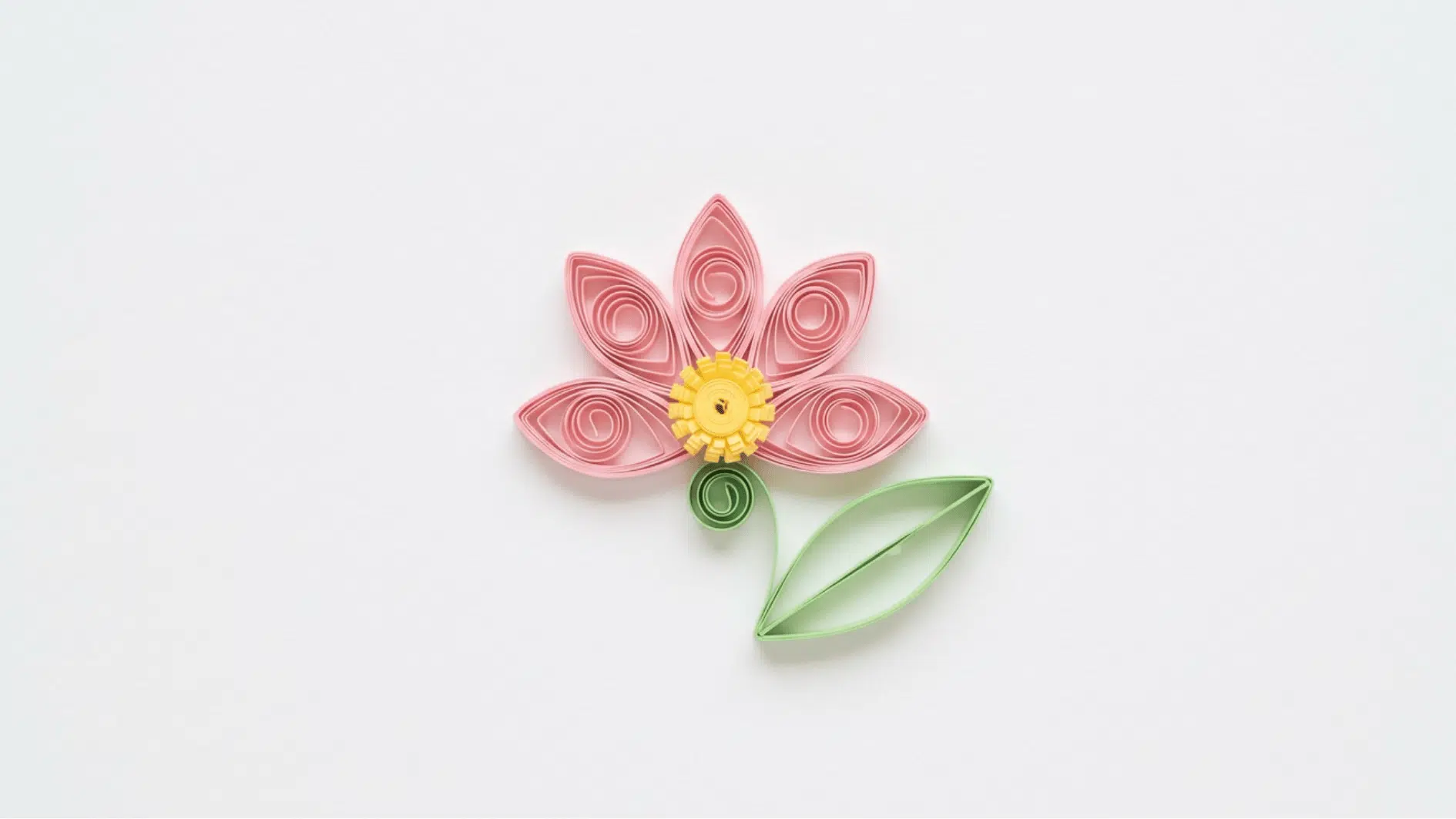 quilled paper flower with pink petals yellow center and curled green stem and leaf on white background