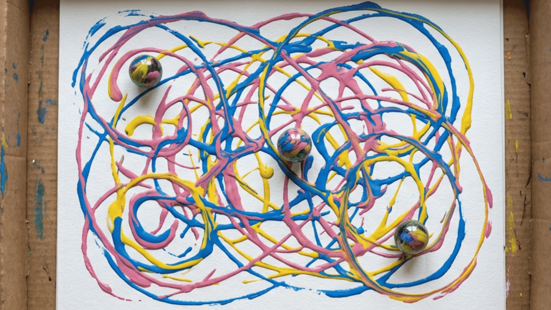 colorful marble painting with pink blue and yellow swirling paint trails in a cardboard box
