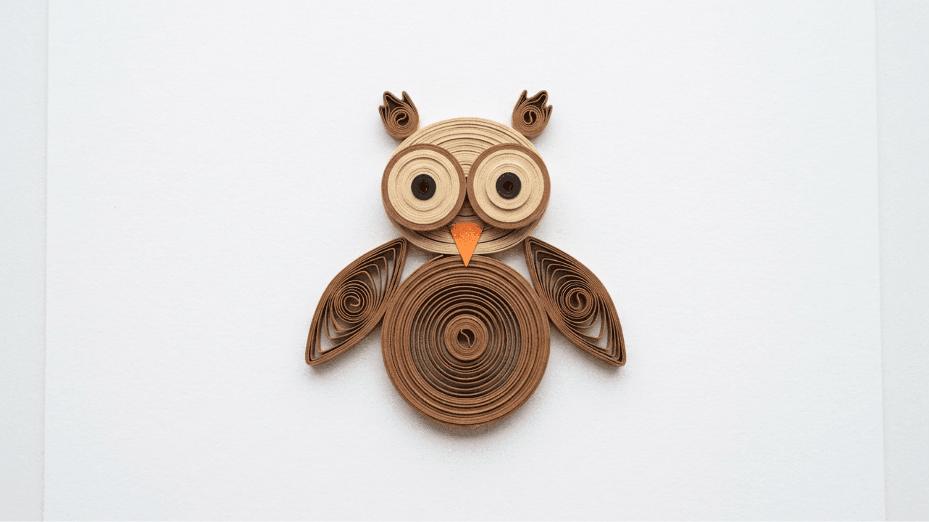 quilled paper owl in brown tones with big round eyes and orange beak on white background