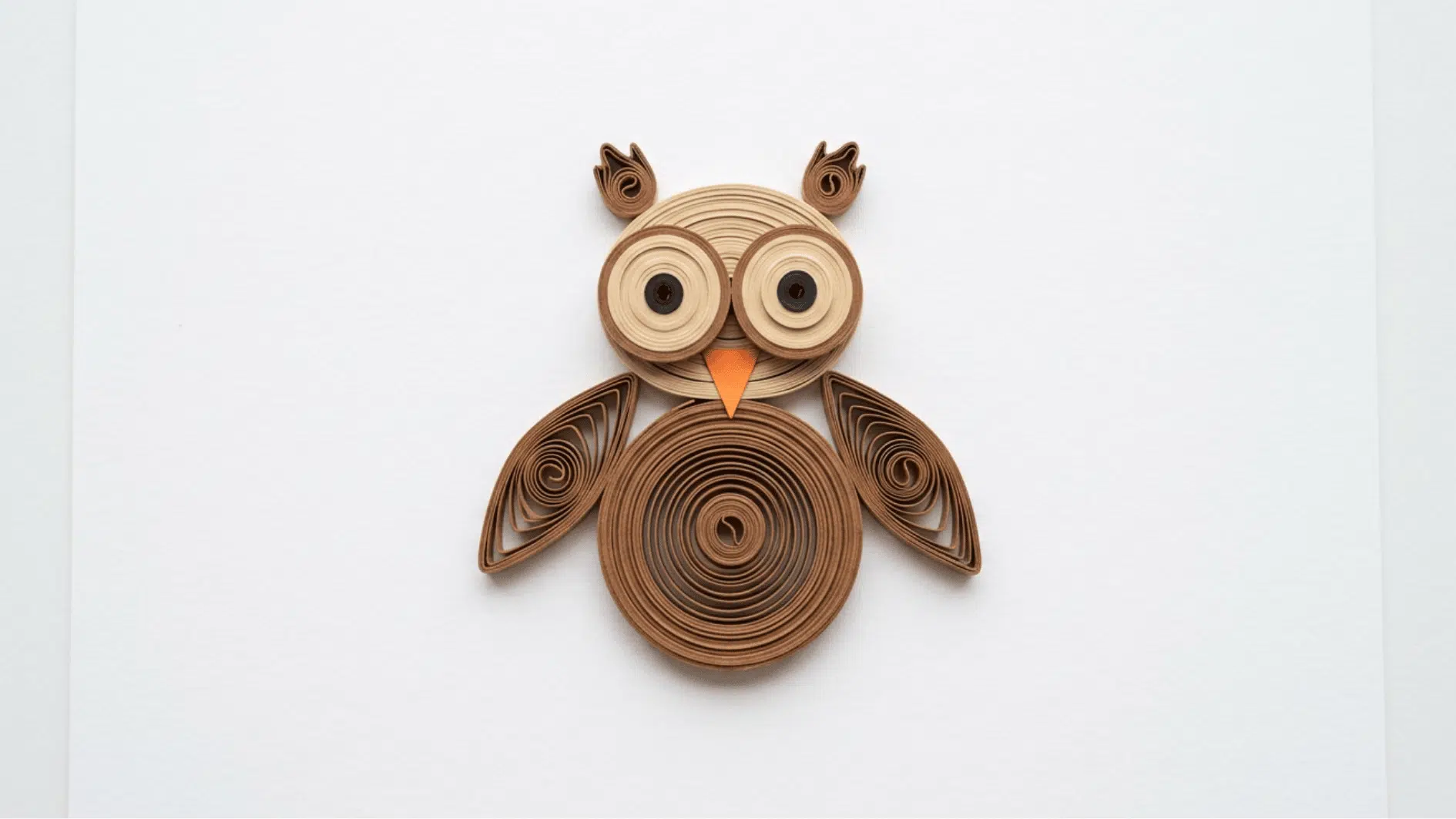 quilled paper owl in brown tones with big round eyes and orange beak on white background