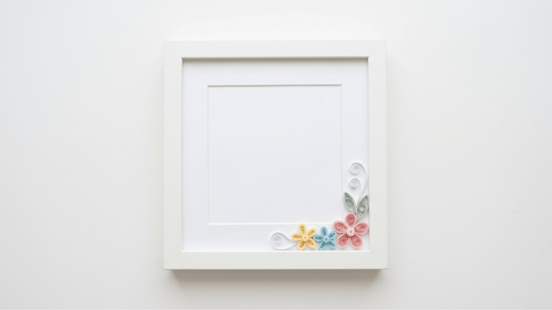 white picture frame with quilled paper flowers in yellow blue and pink in the corner
