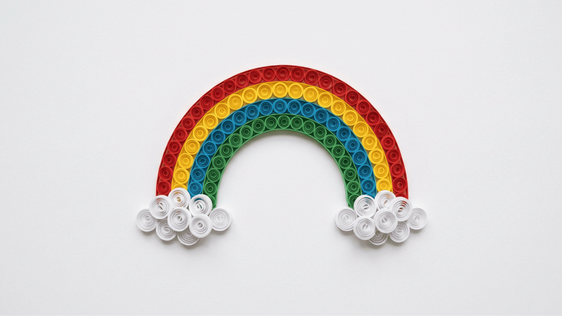 quilled paper rainbow with red yellow blue and green arcs and white cloud coils on white background