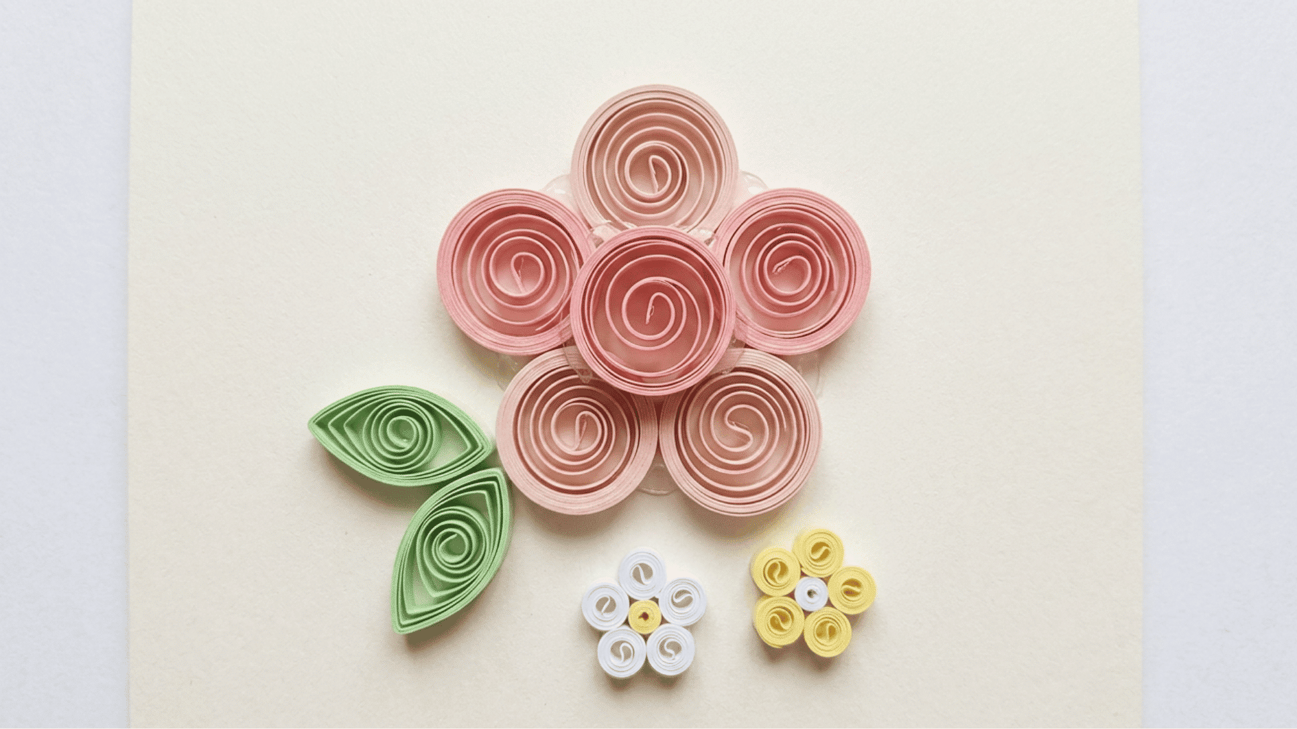 quilled paper flowers in pink with green leaves and small white and yellow flower accents on cream background
