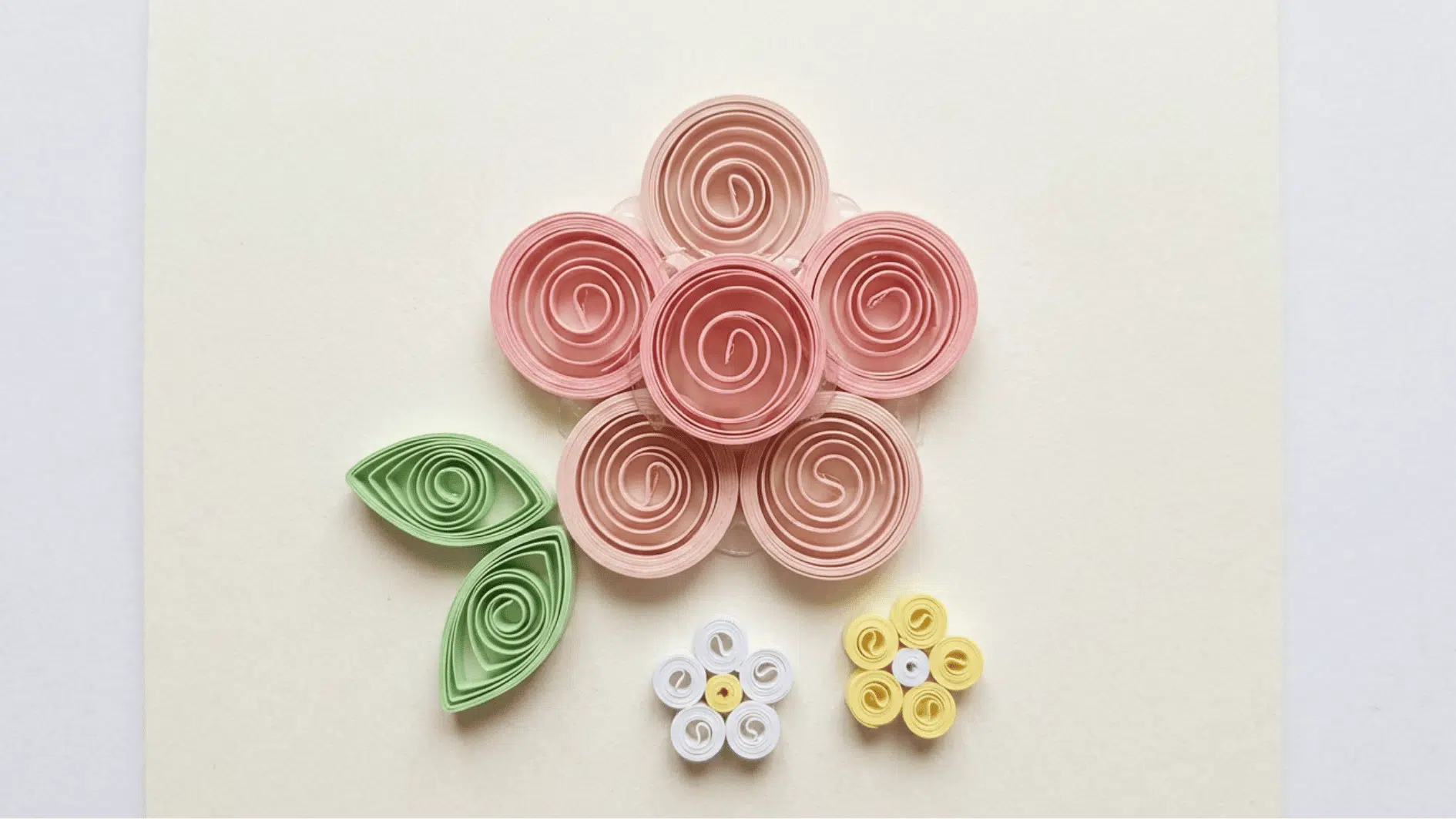 quilled paper flowers in pink with green leaves and small white and yellow flower accents on cream background