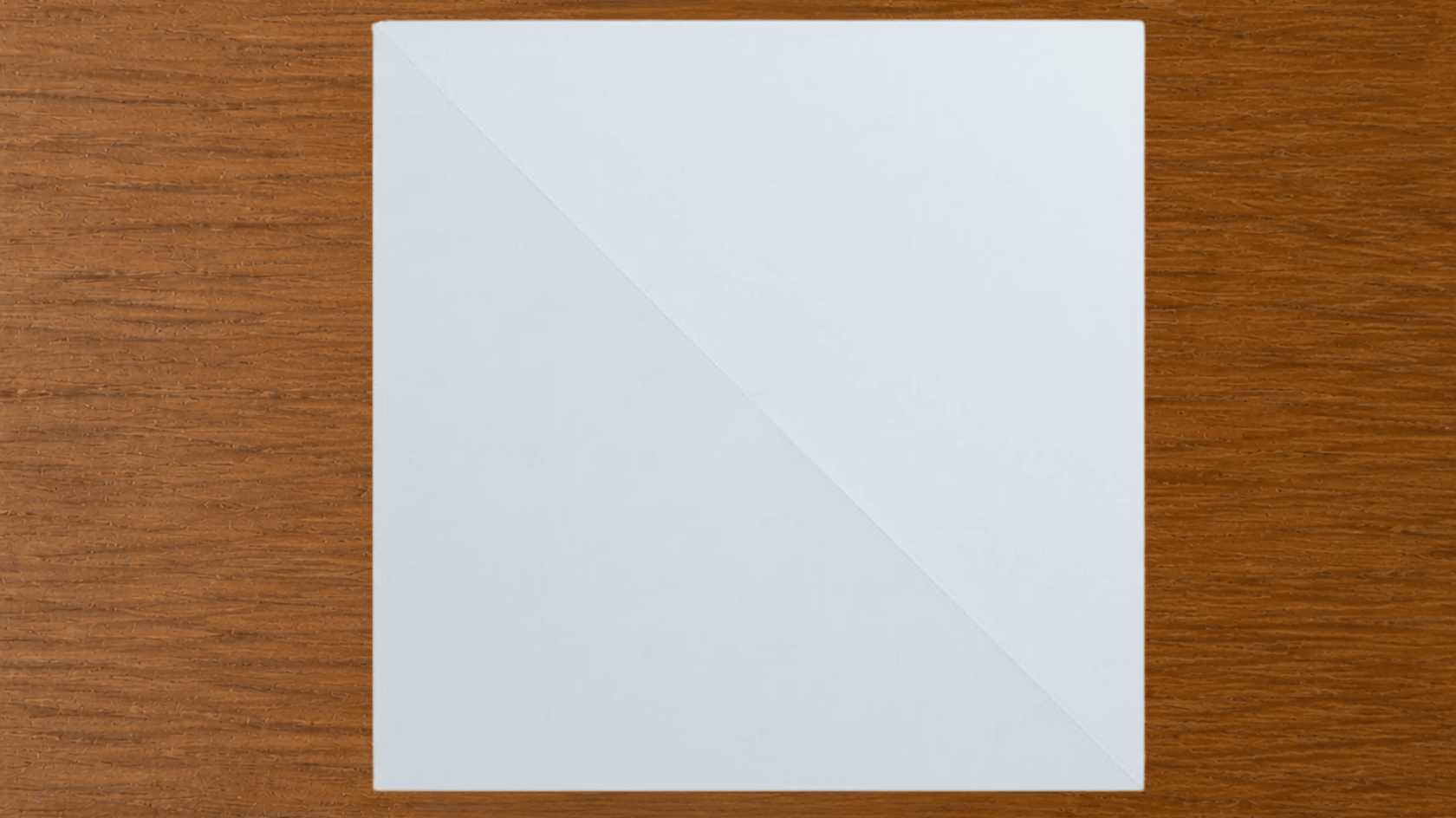 square white paper with a diagonal crease on a wooden surface