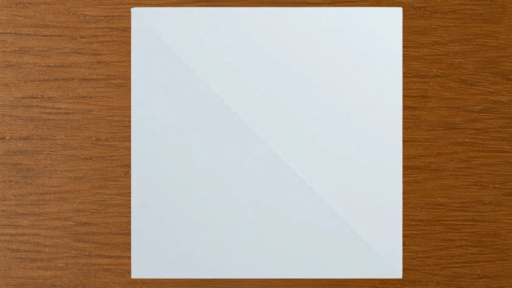 square white paper with a diagonal crease on a wooden surface