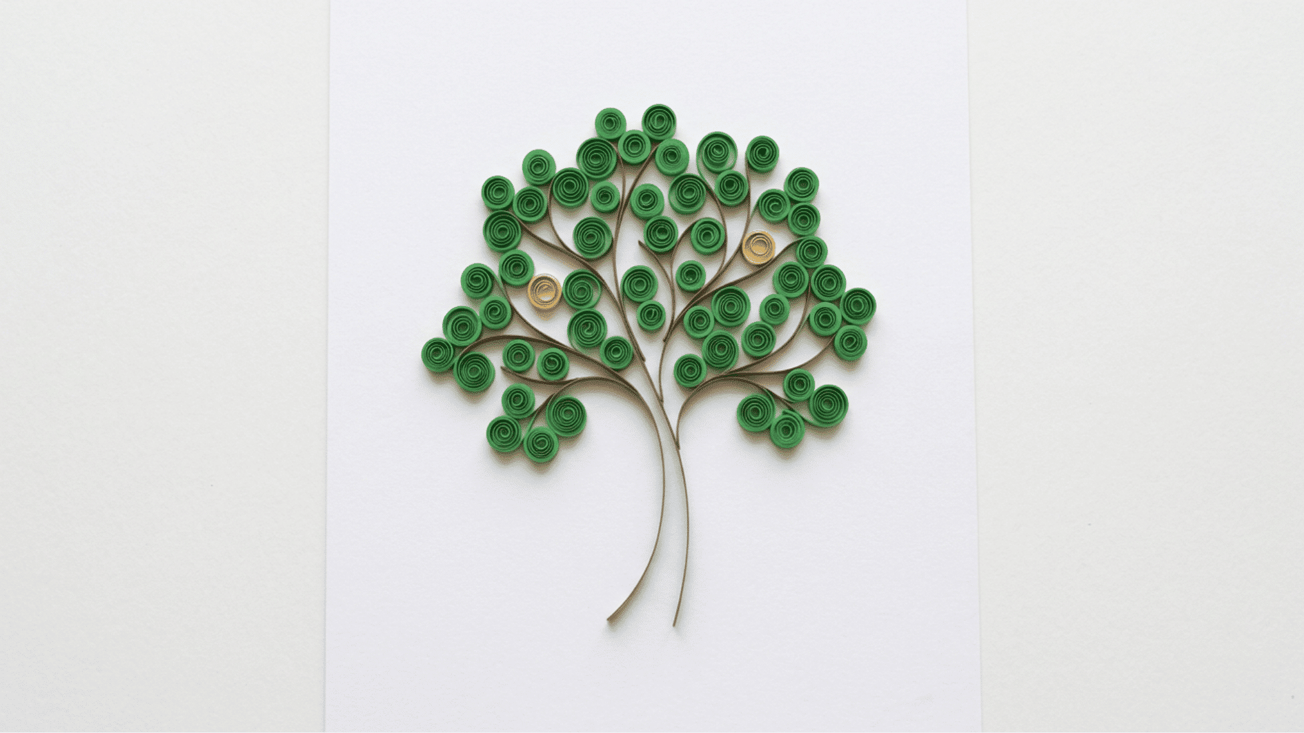 quilled paper tree with green coiled leaves and brown branches and trunk on white background