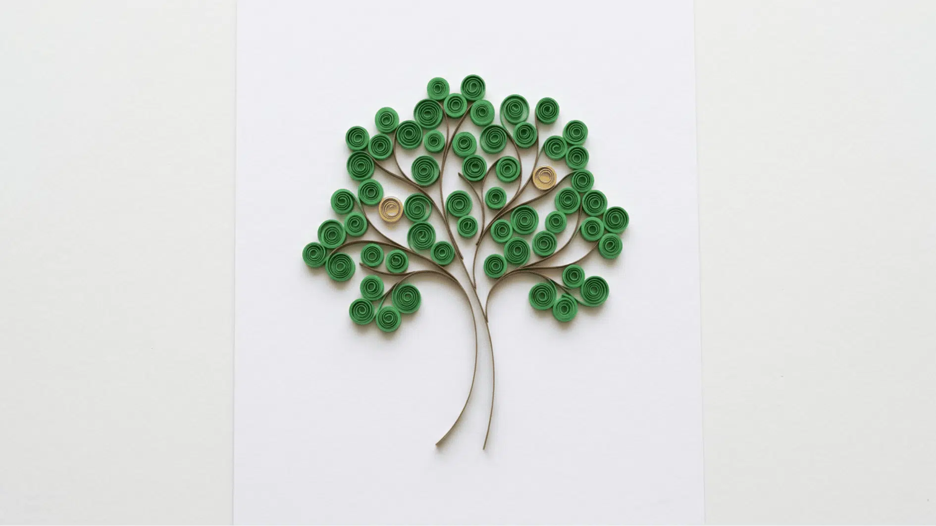 quilled paper tree with green coiled leaves and brown branches and trunk on white background