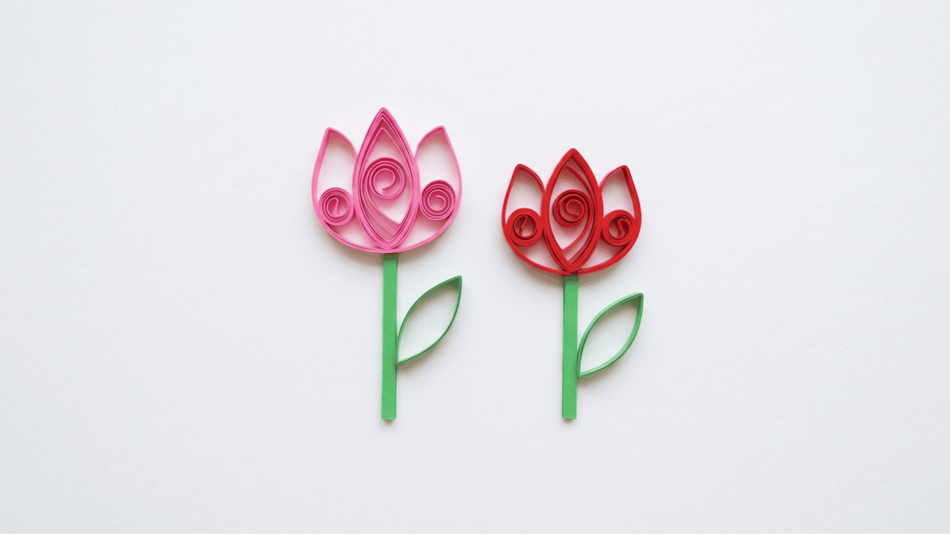 quilled paper tulips in pink and red with green stems and leaves on white background