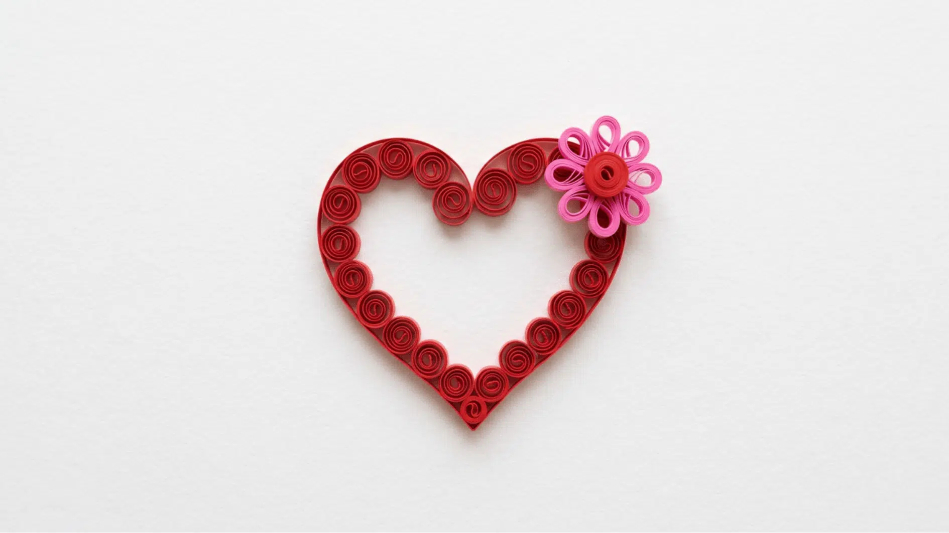 quilled paper heart in red coils with a pink flower accent on white background